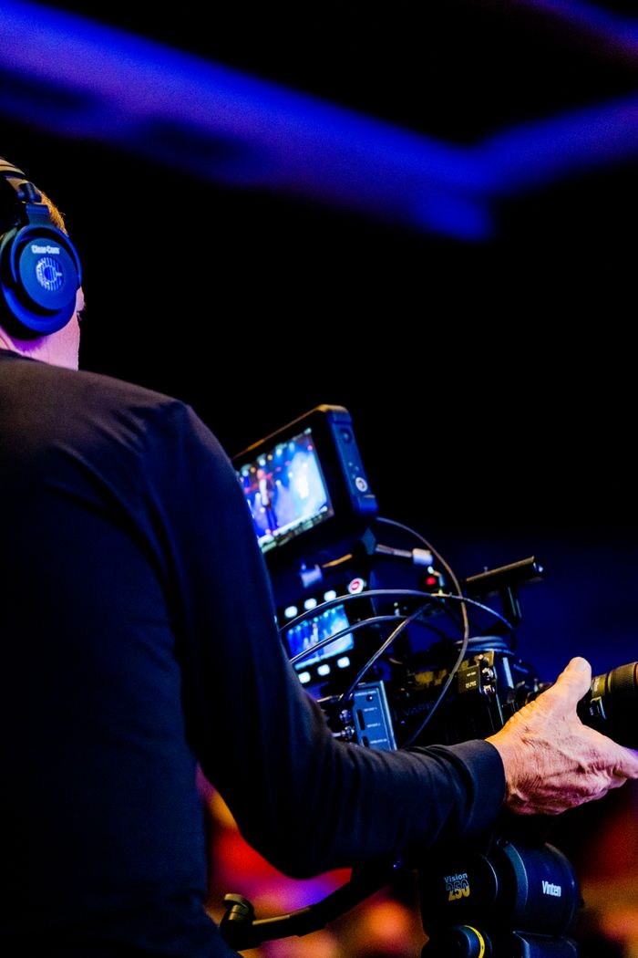 Cameraman using professional equipment to film in a dimly lit studio setting.